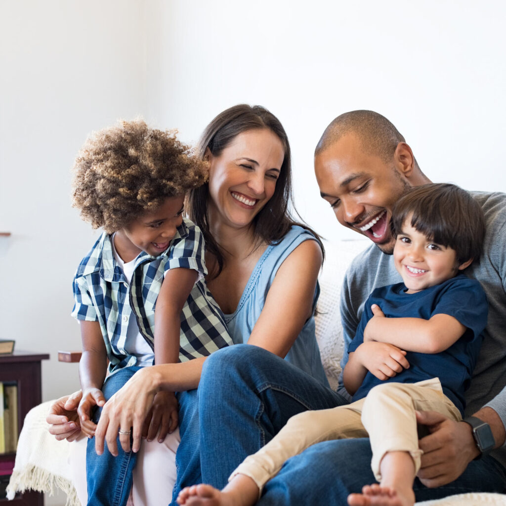 A young family that is all smiles while sitting on a couch to help illustrate Dentist in Norwalk.