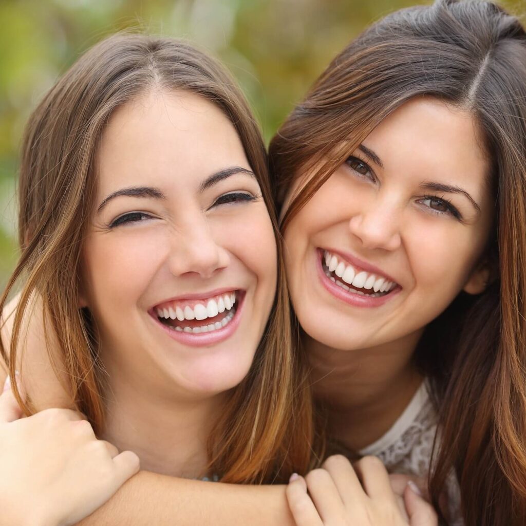 Dentist in Cerritos: Two women smiling, showing off beautiful teeth, to help illustrate esthetic dentistry vs cosmetic dentistry