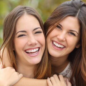 Dentist in Cerritos: Two women smiling, showing off beautiful teeth, to help illustrate esthetic dentistry vs cosmetic dentistry