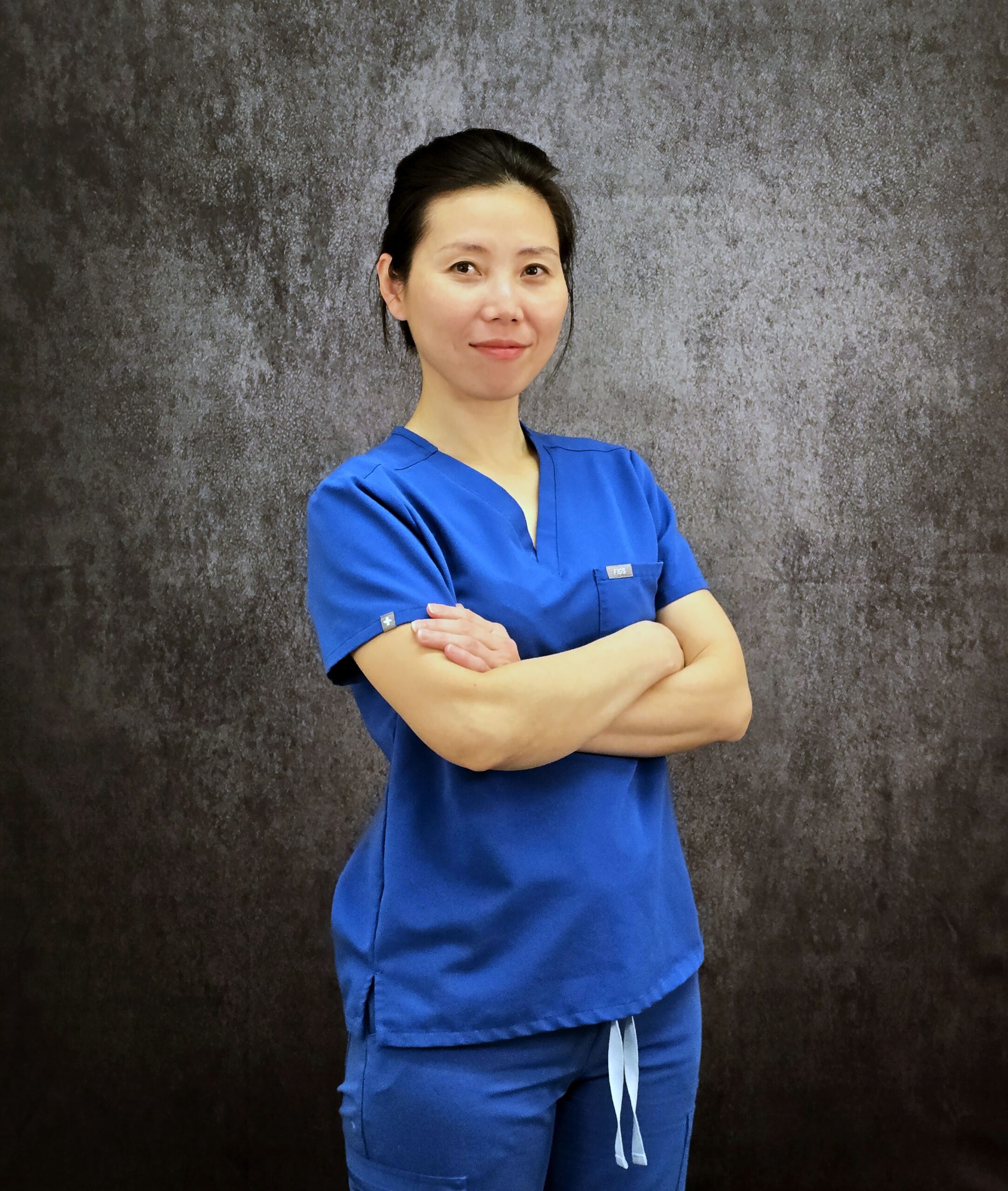 Sabrina Asian Dental Assistant in Blue Scrub smiling with arms crossed.