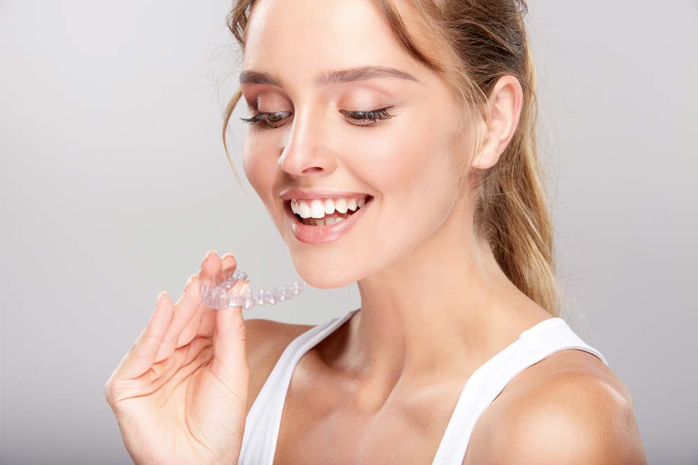 a smiling woman holding invisible Invisalign braces