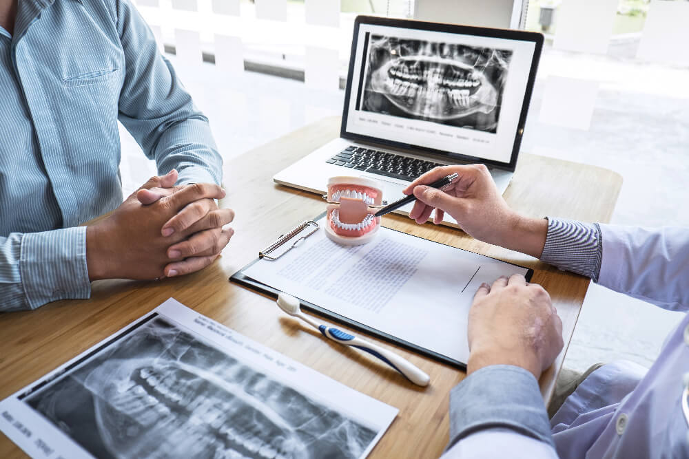 a dentist pointing to a dental model in front of a laptop